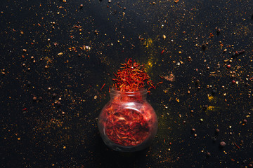 Saffron spice in an open glass jar on dark black background. Seasonings for food. Close-up. Top view