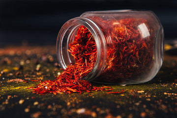 Saffron spice in an open glass jar on dark black background. Seasonings for food. Close-up.