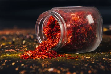 Poster Saffron spice in an open glass jar on dark black background. Seasonings for food. Close-up. © SB