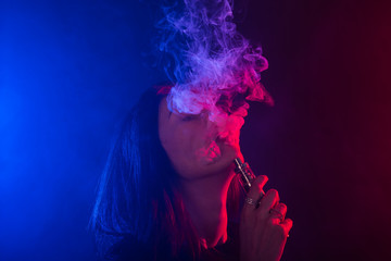 Obraz premium Portrait of girl in colored neon smoke with vape or electronic cigarette.