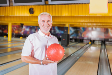 Great mood. Joyful happy man smiling while holding a ball while playing bowling