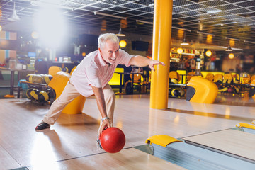Favourite hobby. Delighted cheerful man smiling while enjoying playing bowling