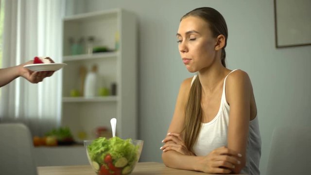 Lean girl choosing between salad and cake, healthy diet vs high-calorie food
