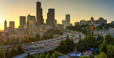 Panoramic view Seattle skylines and rush hour traffic on highway I-90 and I-5 interchange. Nearby density of homeless tents, tiny shelter in trees foreground on the left. Problem of urban life concept - obrazy, fototapety, plakaty