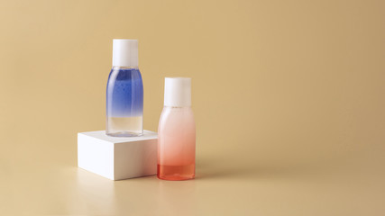 close up view of face wash in bottles on white cube on beige backdrop