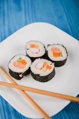 Delicious sushi rolls on white plate with two chopsticks. Blue wooden background.