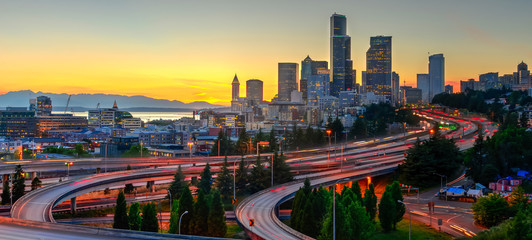 Panoramic view downtown Seattle skyscrapers and I-5 Freeway at I-90 interchange at orange sunset. Long exposure of traffic light trails during rush hour. View from Jose P. Rizal Bridge (12th bridge)