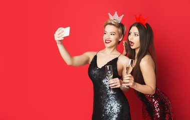 Happy girls in party dresses and tiaras making vlog on smartphone
