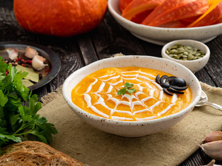 Funny food for Halloween. Pumpkin puree soup, spider web, dark old wooden table, side view.
