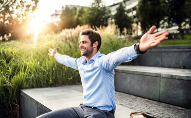 A happy young businessman with arms stretched outdoors at sunset. - Powered by Adobe