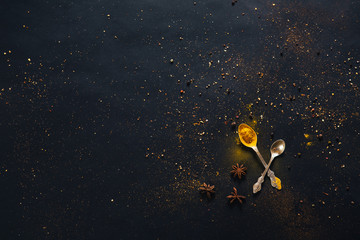 Assorted spices in spoons with empty space for text on dark black background. Seasonings for food. Curry, paprika, pepper, cardamom, anise, cloves, turmeric. Top view. Close-up.