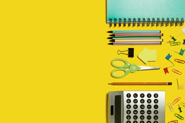 multiple school and office suplies and gadgets lying diagonally on a yellow background. free space...