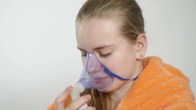 Teenage girl using nebulizer with breathing mask at home inhaling the medication