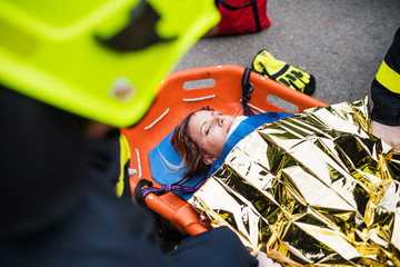 An injured woman in a plastic stretcher after a car accident, covered by thermal blanket.