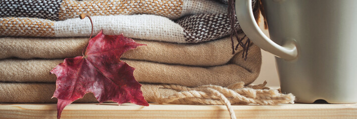 stack of beige checkered wool blankets, autumn maple leaf and cup on a wooden chest. concept of...