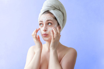 Beauty portrait of a smiling brunette woman in a towel on the head applying white nourishing mask...