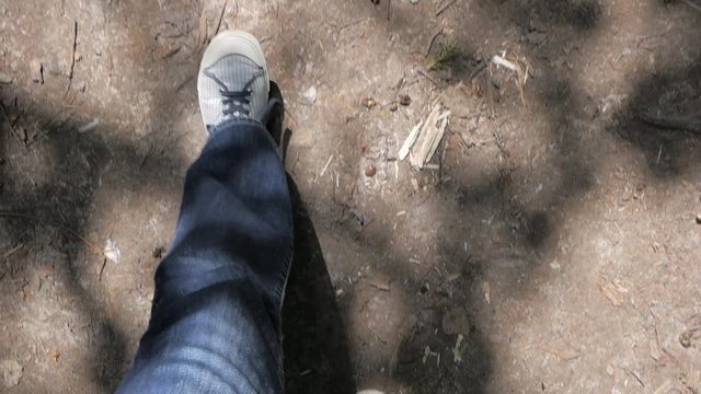 Legs in jeans and striped blue and white snickers walking forward on brown earth. Top view.