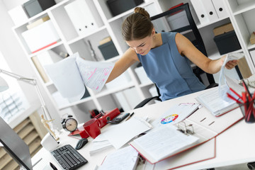 A young girl sits in the office at the computer desk and dismantles the mountain of documentation.
