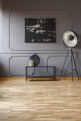 Black painting on grey wall with molding in living room interior with lamp next to table. Real photo