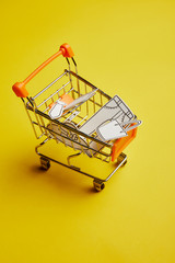 close up view of little shopping cart with clothes made of paper on yellow background