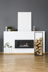 Firewood and silver table in front of fireplace in loft interior with mockup of white empty poster....