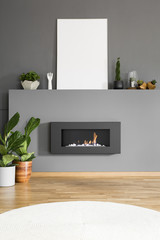 Mockup of white empty poster above fireplace in grey living room interior with plants. Real photo
