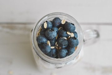 Jar with overnight oats and fresh blueberry on wooden table, top view. Homemade yogurt with fruits. Breakfast meal