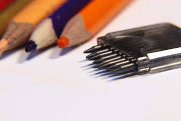 A graphite into a compass. Colourful crayons on white background. Neccessary accessories to school