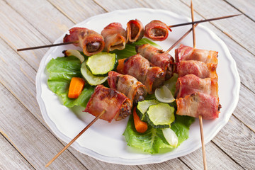 Chicken liver wrapped with bacon on skewers. Grilled liver kebabs with vegetables
