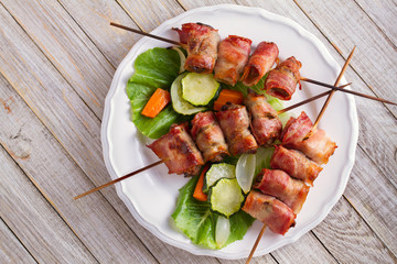 Chicken liver wrapped with bacon on skewers. Grilled liver kebabs with vegetables. View from above,...