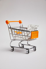 close up view of shopping cart with little clothes made of paper on grey background