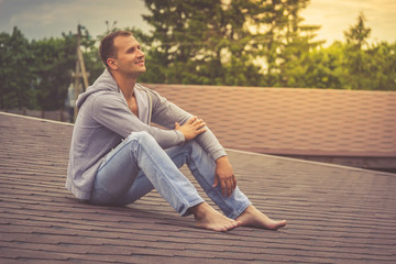 Obraz premium Barefoot Attractive young boy is sitting on the roof and dreams