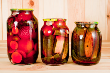 Canned tomatoes and cucumbers in a glass jar on a wooden background