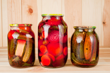Canned tomatoes and cucumbers in a glass jar on a wooden background