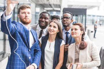 Obraz premium Self portrait of stylish successful, professional team, afro-american black man with stubble shooting selfie with hand on smart phone with friends, together standing in work place, station