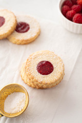 Christmas cookies. Linzer cookies with raspberry jam on white table background. Traditional Austrian biscuits filled. Top view and copy space