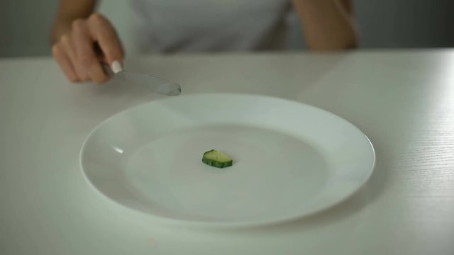 Girl slicing cucumber, obsessed with undereating, fear of overweight, anorexia