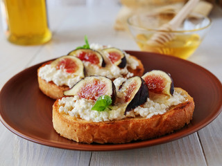 Bruschetta toast topped with goat cheese, fig slices, honey and herbs over wooden table