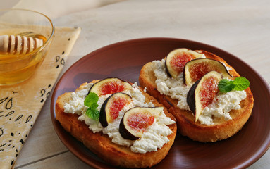 Crostini toast topped with goat cheese, fig slices, honey and herbs over wooden table