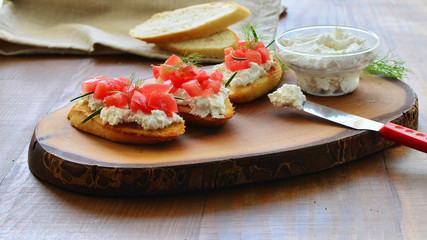 Crostini toast with creamy cottage cheese spread, chopped tomatoes and herbs over wooden board