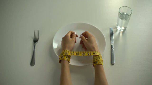 Hands tied with tapeline on empty plate, girl obsessed with counting calories