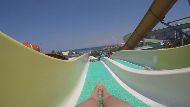 Two happy female friends roll in parallel on a slide in water park