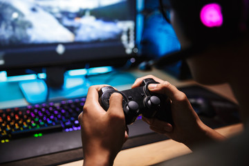 Photo closeup of asian gamer boy playing video games online on computer in dark room, wearing headphones with microphone and using joystick © Drobot Dean