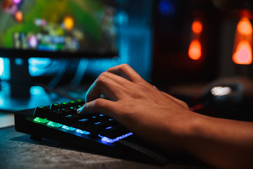 Hands of professional gamer man playing video games on computer in dark room, using backlit...