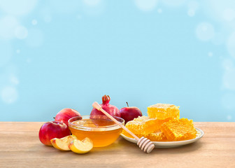 Honey in glass bowl, wooden honey dipper and honeycombs, red apples and garnet on wooden table on a...