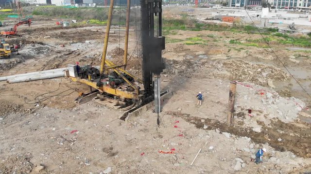 High view of pile driver rig at construction site. Drone aerial shot of heavy construction equipment building foundations for building skyscraper. High impact weight drives pole deep into the ground.
