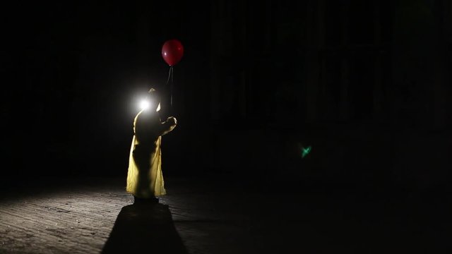 Male silhouette in yellow cloak with red balloon in his hand in dark