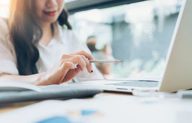 Young asian casual business woman holding pencil in hand while working with laptop computer on table