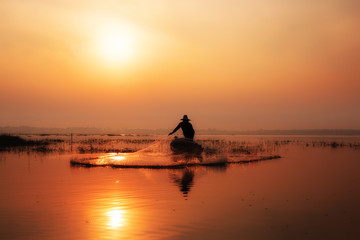 Silhouette of fishermen casting for catching the fish on the wooden boat at the lake in the morning