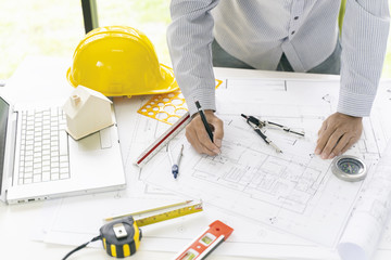 Top view, Architect or engineer hands working on blueprint plans with a pencil ,laptop a ruler, calculator, and engineering tools. Architect or engineer working on blueprint in office.